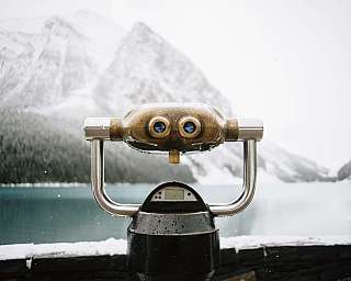 Fernrohr mit Blick auf verschneite Berge und See im Hintergrund