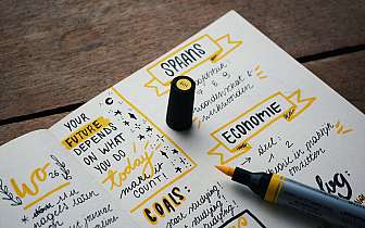 Offenes Notizbuch mit handgeschriebenen Notizen und gelbem Marker auf Holzoberfläche